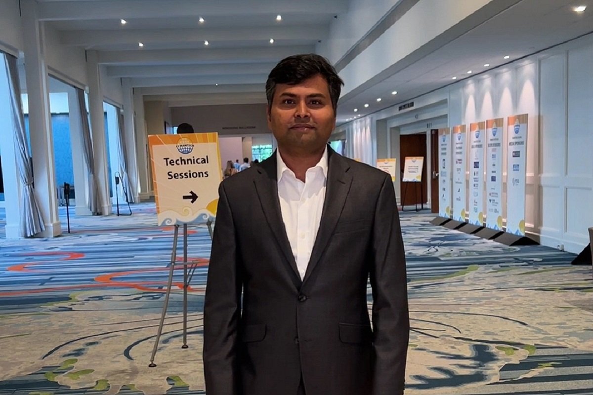 Prakash Sundaram dressed in a dark suit standing in hallway smiling into camera