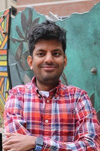 Sidhharth Raju outdoors in a red plaid shirt against a green backdrop