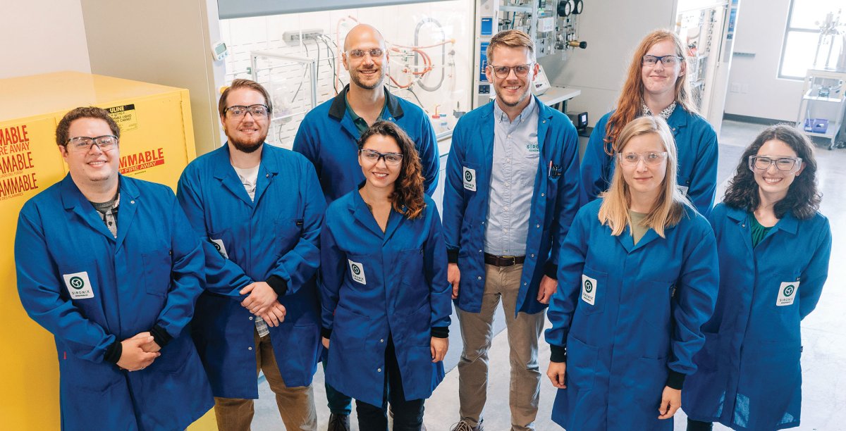 A group of people in blue lab coats standing in a bright lab