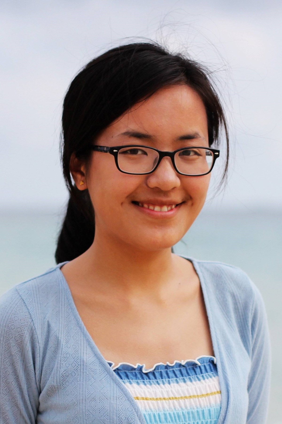 Yang (Katie) Zhao standing outdoors in a blue blouse and sweater smiling into the camera