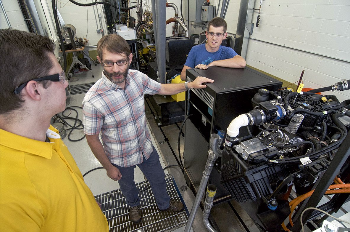 A professor and two students standing in front of an engine.