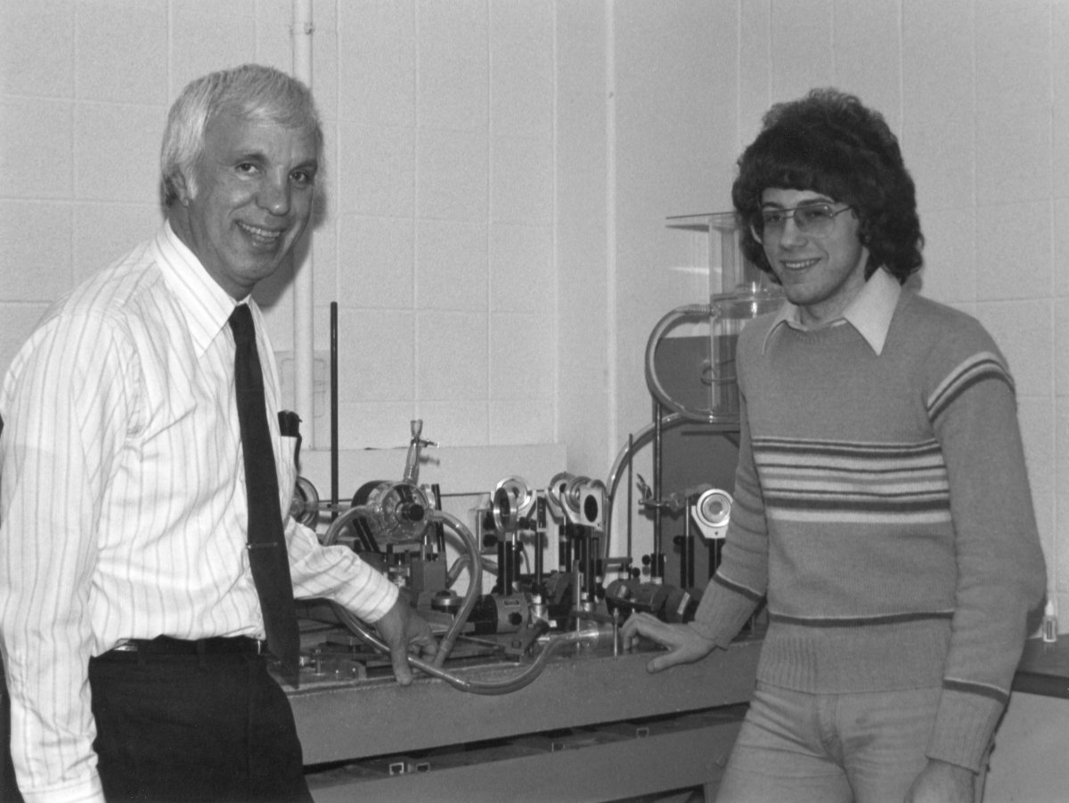 Dick Goldstein stands next to machine with student