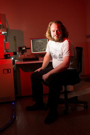 Nick Seaton sitting, posing next to microscope