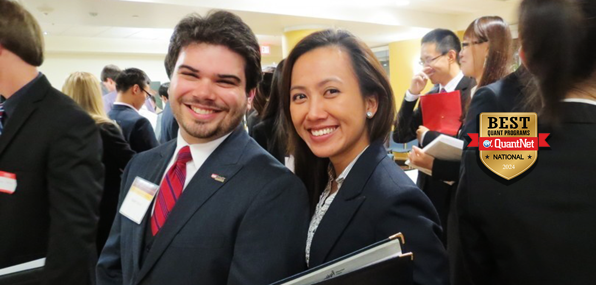 Two students in suit jackets stand in a crowd and smile at the camera.