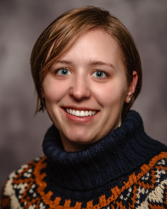White woman with short light brown hair wearing a turtleneck sweater on a dark grey background
