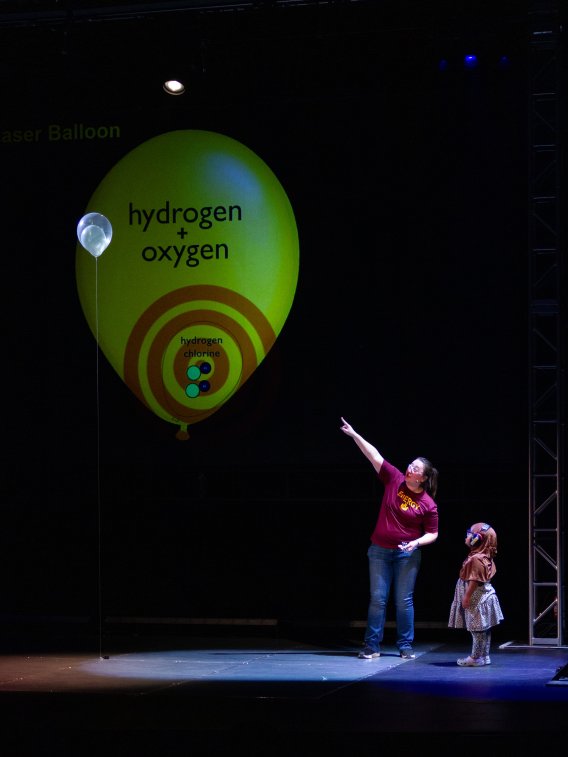 Jessica Lamb stands on stage with a student, pointing to a balloon.