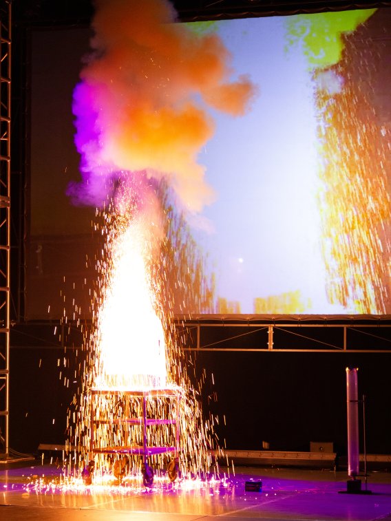 A bright yellow and orange explosion shoots off sparks on a darkened theater stage.