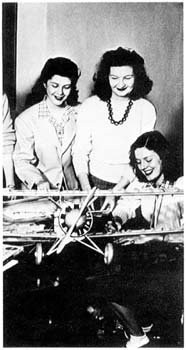 Three women in front of a model airplane.
