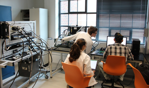 students sit around a computer with lab equipment in the room