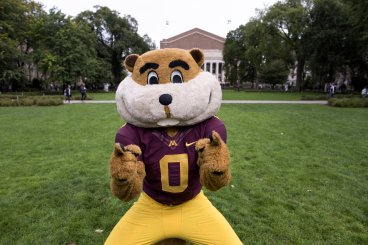 Goldy points to the camera wearing a football uniform on the main mall