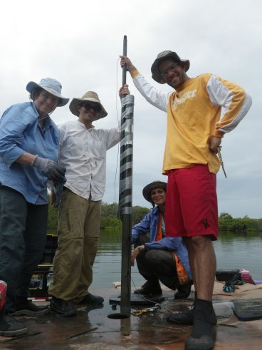 4 people standing around a coring tube secured to a rod using duct tape.
