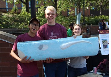 Three students hold protion of concrete canoe