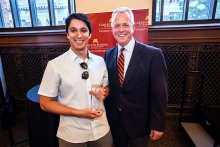 Aditya Prabhu in a pale blue shirt holding a glass plaque. Prabhu is standing next to John Stavig, the director of Holmes Center for Entrepreneurship. Stavig is dressed in a dark suit with a maroon and gold tie