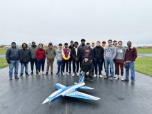 image of small blue airplane in foreground with line of students in the background on tarmac
