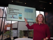 A woman in a red dress smiles and points to a Powerpoint slide behind her