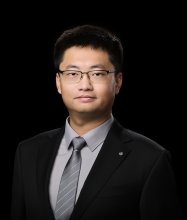 Headshot of Asian male wearing a black suitcoat and grey tie and shirt on a black background
