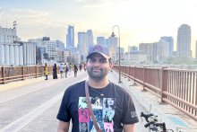 Sai Sanjay Balaji wearing a dark T-shirt standing on a bridge against the backdrop of the Minneapolis city skyline the bacdrop of 