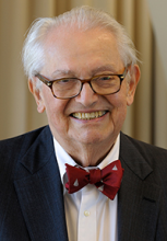 Person with glasses wearing a suit and red bowtie