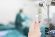 hand changes the rate on an IV with doctor in the background
