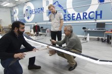 researchers talking while holding parts of a solar-powered UAV