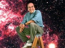 Saul Perlmutter sitting on a ladder with a galaxy background behind him