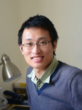 Zhen Liu, a man with dark hair and glasses wearing a green button down shirt and blue sweater.