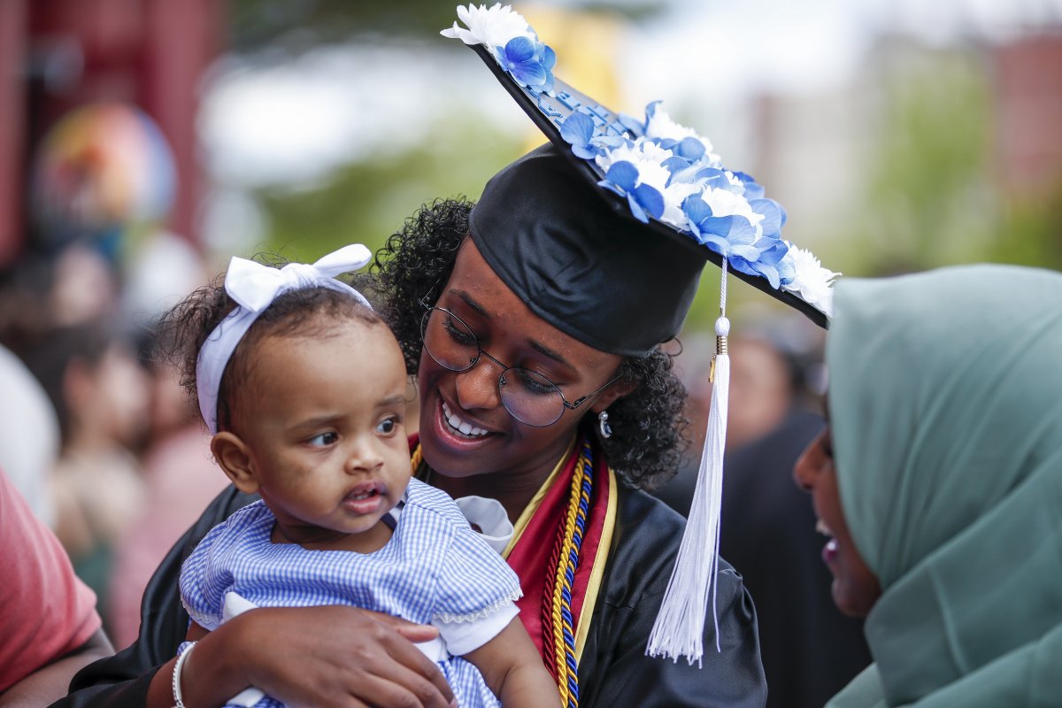student in mortar board at graduation holds a small baby