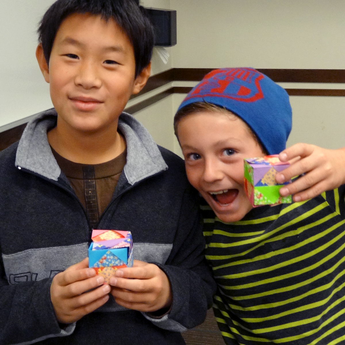 Two young students excitedly hold up orgami cubes
