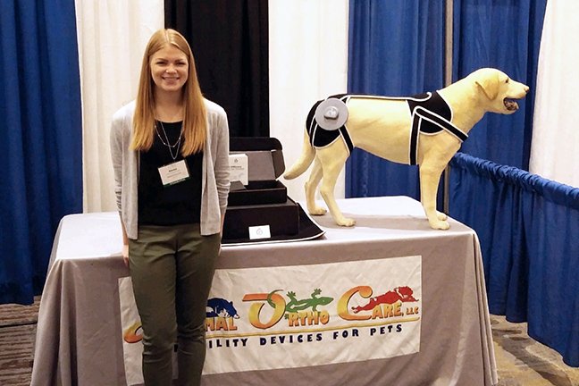 A student standing next to a table with a model dog wearing a brace.
