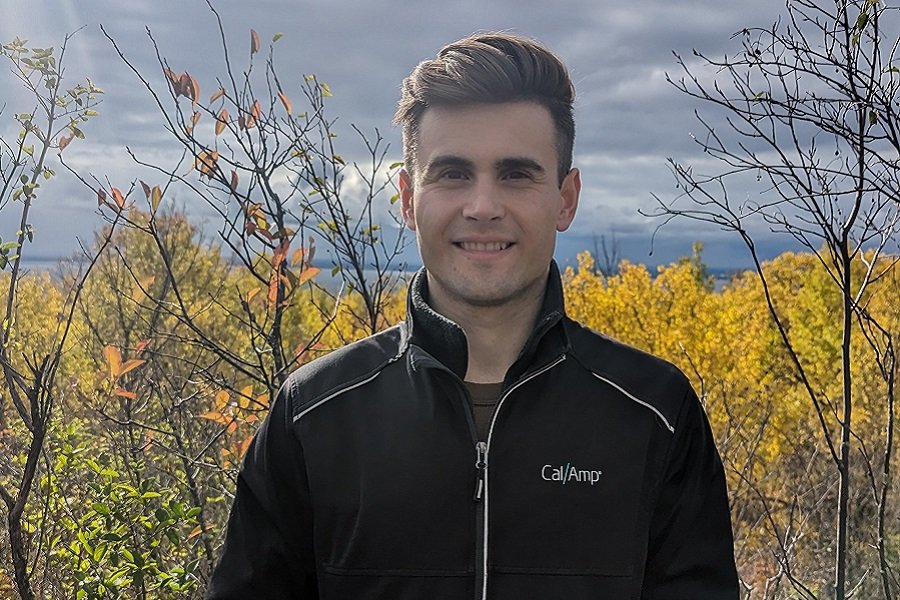 Alex Wege in a dark zip-up shirt standing outdoors smiling into camera