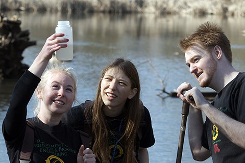 students in the field by a lake looking at a water sample
