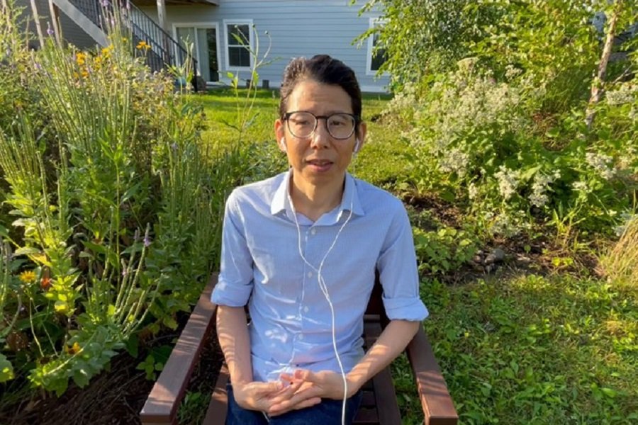 Professor Chris Kim sitting outdoors in a garden smiling into camera