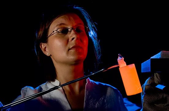 Emilia Morosan a woman holds a glowing beaker in a pair of tongs.