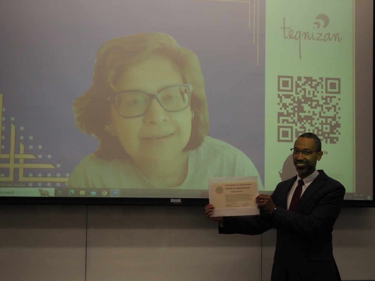 A man holds a certificate up as a woman projected on a large screen smiles behind him