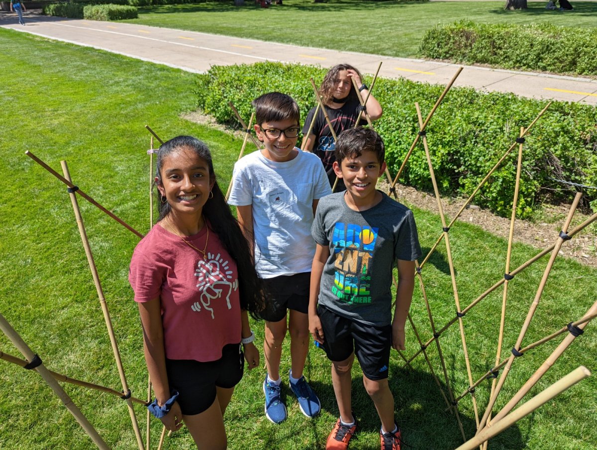 Four students on the U of M campus lawn standing around geometric shapes constructed from bamboo