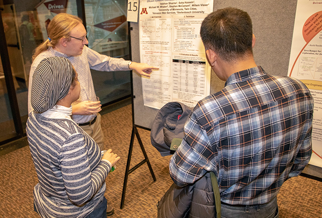 A student presenting their poster to two on-lookers