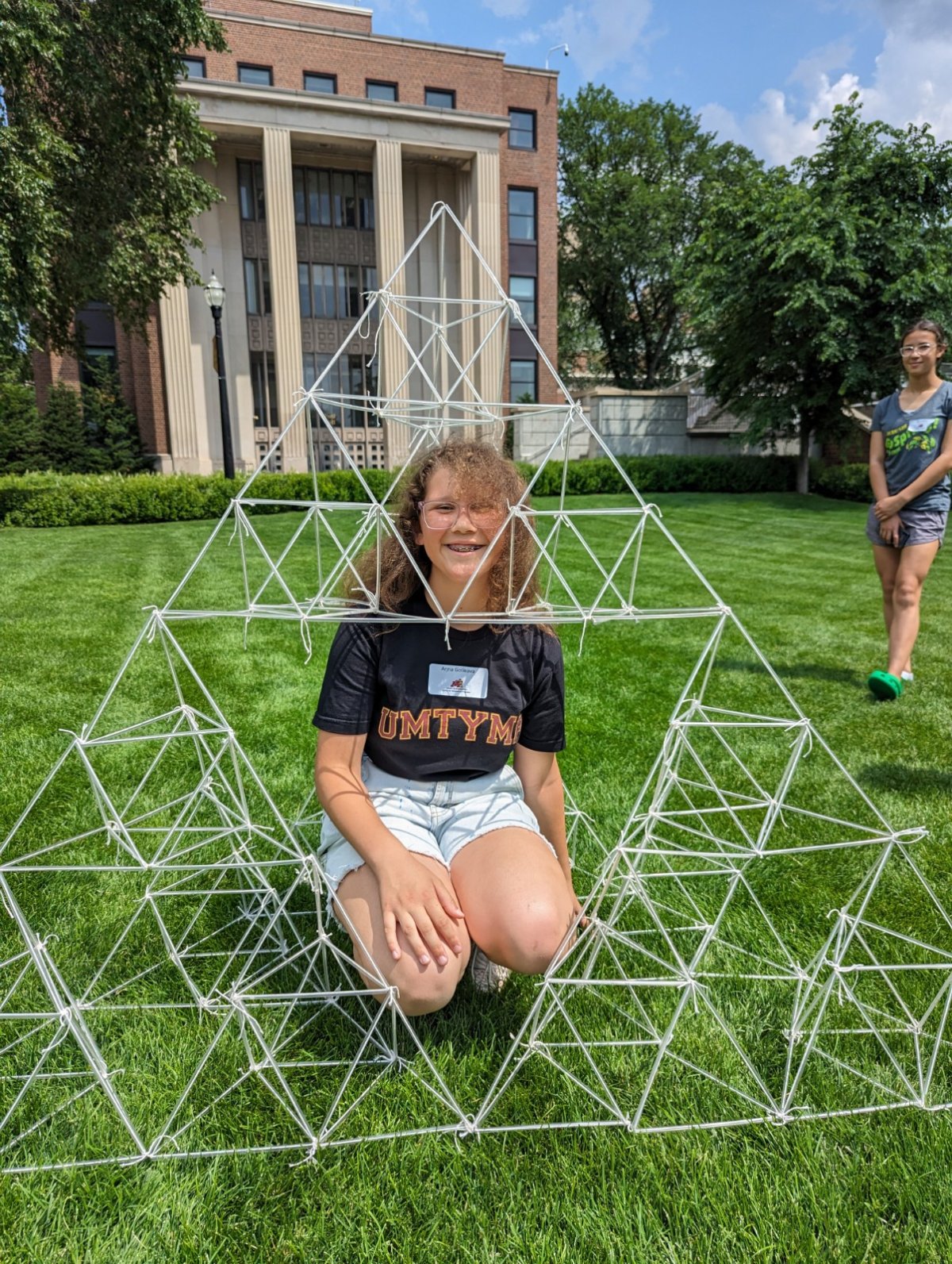 Student on the U of M campus lawn sitting inside a pyramid made of straws