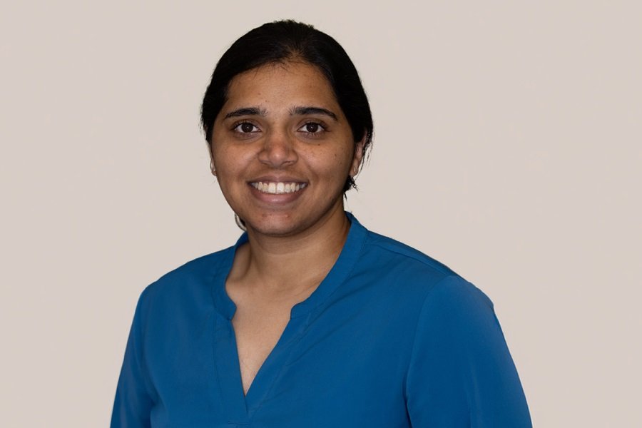 Vidya Chhabria in a blue shirt standing against a beige wall smiling into camera
