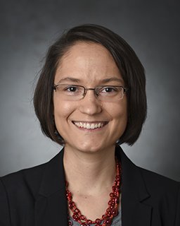 A headshot of Allison Beese. She wears glasses and stands in front a gray backdrop.