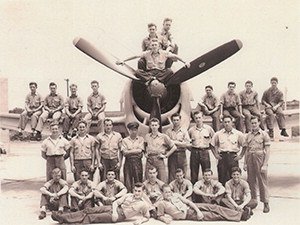 black and white photo of cse alumni posing with a war plane