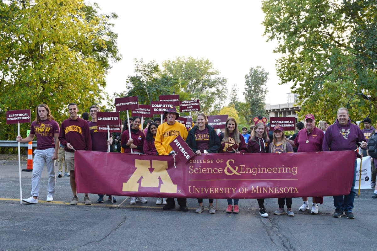 A group of alumni holding department signs and a CSE banner. 