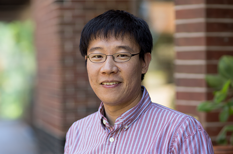 A headshot of of Xiang Cheng. He wears square glasses and a red and white stripped button up.